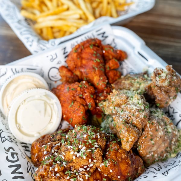 Three varieties of King's Chicken Wings with dipping sauces and fries in the background.