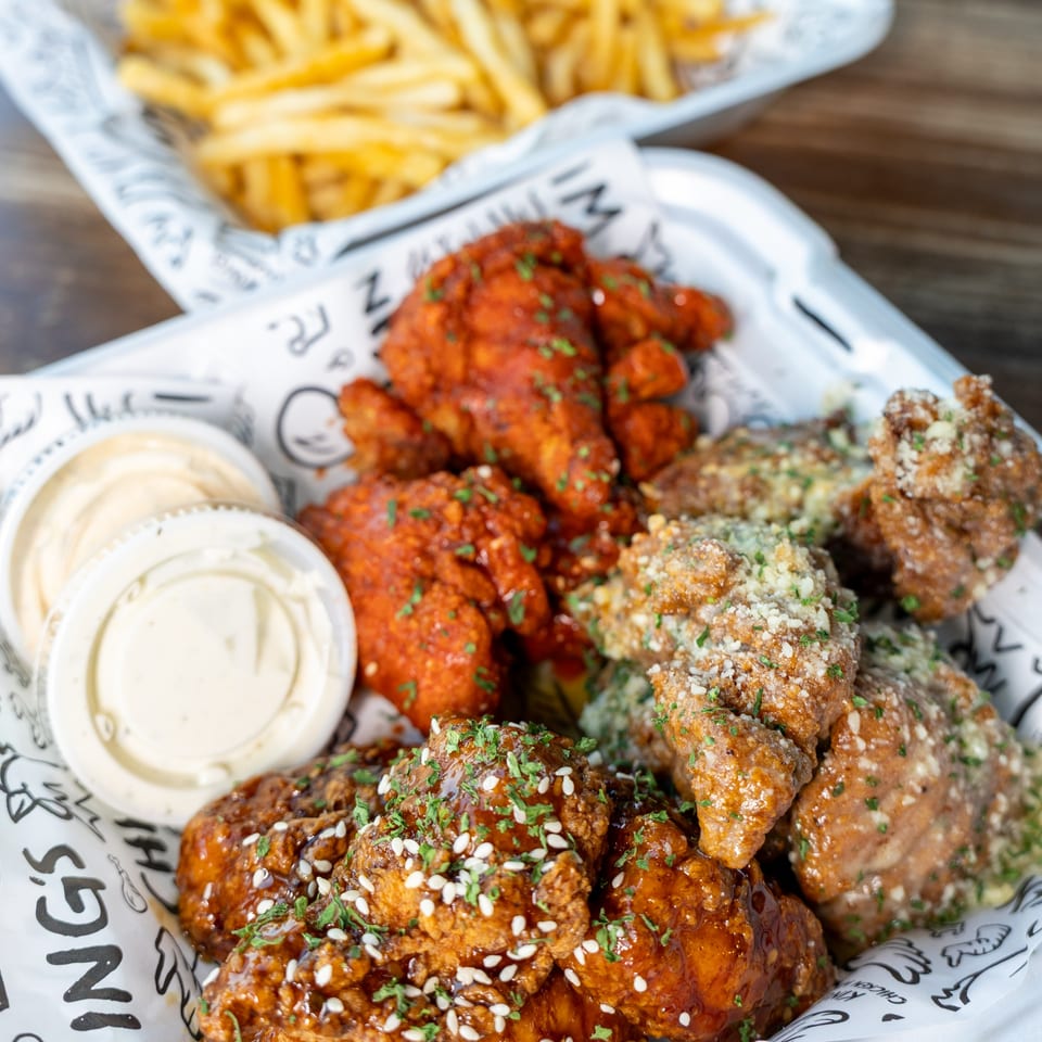 Three varieties of King's Chicken Wings with dipping sauces and fries in the background.