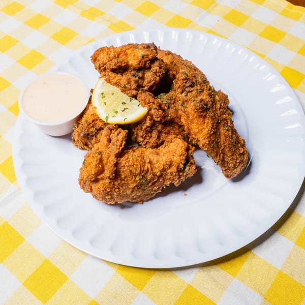 Crispy fried chicken wings with a lemon wedge and dipping sauce on a white plate, on a yellow and white checkered tablecloth.