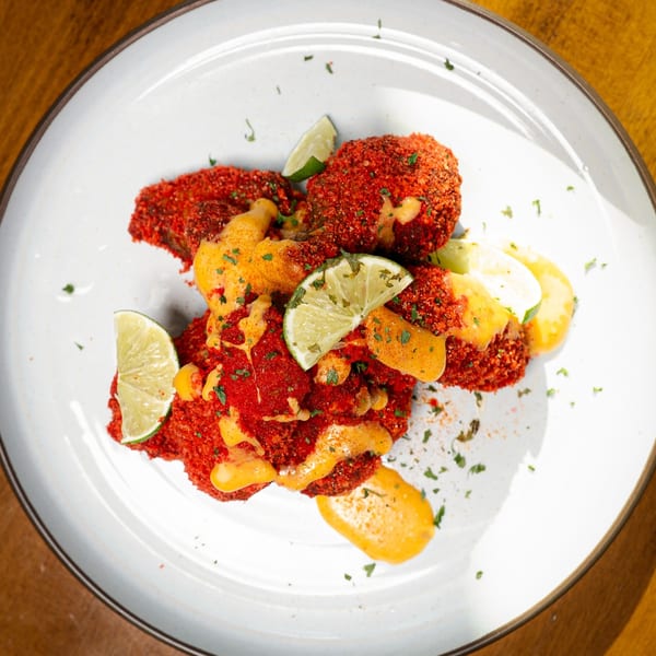 King's Chicken Wings' bright red, crispy wings with orange sauce, lime wedges, and parsley on a white plate.