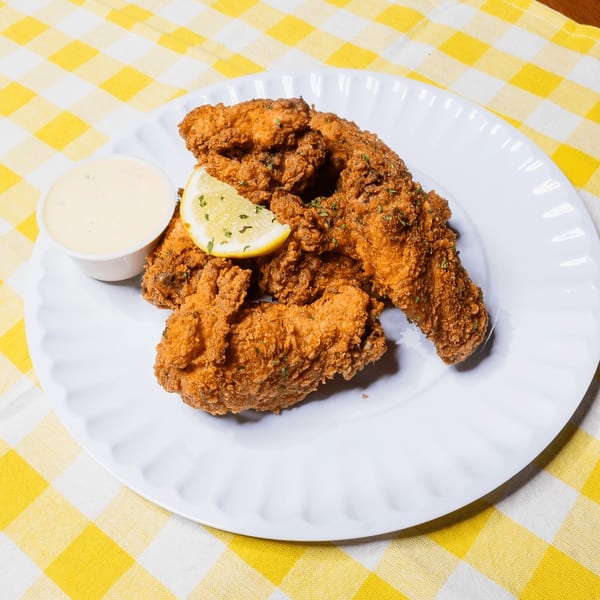 King's Chicken Wings fried chicken tenders with a lemon wedge and dipping sauce on a white plate.