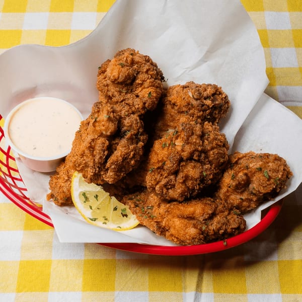 Crispy fried chicken wings with a lemon wedge and dipping sauce in a red basket on a yellow checkered tablecloth.
